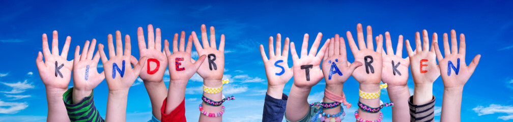 Children Hands Building Colorful German Word Kinder Staerken Means Strengthen Children. Blue Sky As Background
