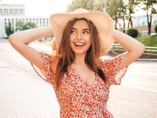 Portrait of young beautiful smiling hipster girl in trendy summer sundress.Sexy carefree woman posing on the street background in hat at sunset. Positive model outdoors