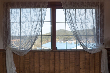 Old wooden window with white lace curtains.