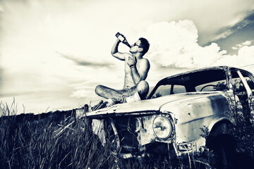Young guy drinking a beer on an old car