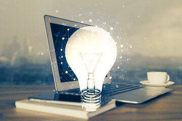 Computer on desktop in office with bulb icon hologram. Multi exposure. Concept of idea.