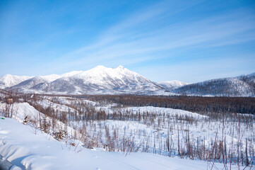 Scenic winter landscape of mountains and forest covered in snow on sunny day on the Kolyma Highway (Road of Bones). Adventure travel in Russia from Yakutsk to Magadan