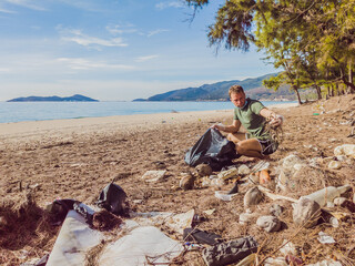 Man in gloves pick up plastic that pollute sea and forest. Problem of spilled rubbish trash garbage on the beach sand caused by man-made pollution, campaign to clean volunteer in concept