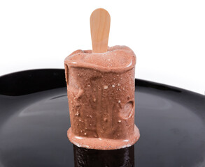 Slightly thawed chocolate ice cream on stick on black dish
