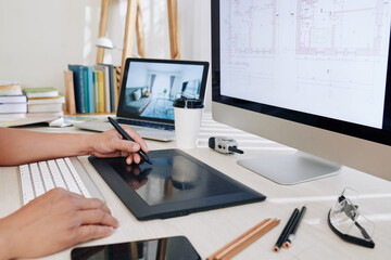 Cropped image of architect working at office desk and using graphic tablet when drawing house...