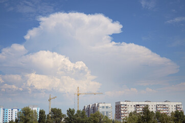 Powerful cumulus clouds in a bright blue sky over tower cranes and multistory houses. View of a new development in an old residential area of the city.