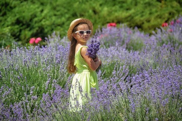 Portrait of a little girl in lavender . A child on a summer walk in a straw hat and sunglasses