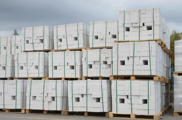 Pack of white silicate bricks on wooden pallets against the blue cloudy sky. Closeup stack in 3 rows.