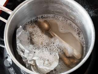 workshop for cleaning tarnished silver with aluminum foil and baking soda - silver spoons in boiling solution of baking soda with aluminum foil in pot on electric stove