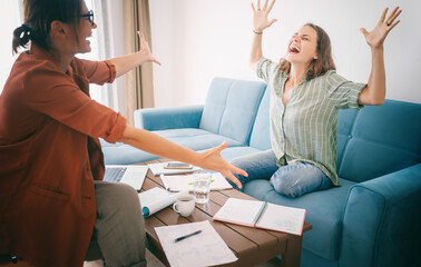 Two young women work at home on a project, happy people celebrate success
