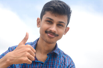 Young teen man showing thumbs up action on sky background.