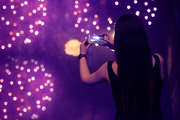 Girl makes a photo of a salute on the phone. Holiday, fireworks. Application for processing photos.