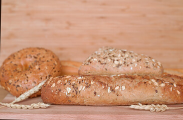 Different types of bread, fresh pastries in the bakery. Bread with sesame seeds, cereals, seeds. Different forms and types of rolls. Wheat ears on a wooden board.