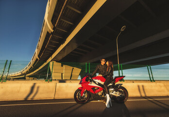 Young couple riding the red sports motorcycle at bridge on sunrise