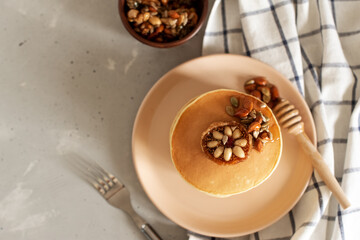 Stack of delicious pancakes with chocolate, honey, nuts and slices of banana on plate and napkin on wooden background