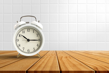 White vintage classic alarm clock on wooden table on white ceramic tile background.