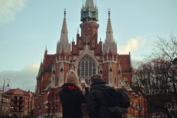 Fototapeta na wymiar A couple traveling to Krakow takes a photo on the phone. The cold season. Couple makes photo of church in historical city