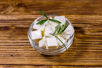 Chopped feta cheese and rosemary in glass bowl on a wooden table