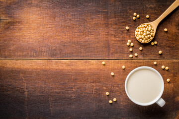 Top view of soy milk in white cup healthy menu And soy beans on wooden spoon with copy space on wooden background.