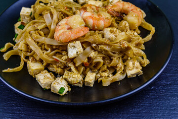 Black plate with pad thai on a slate board