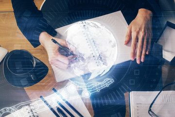 Double exposure of hands making notes with world map hologram and data theme icons. Concept of global computer data.
