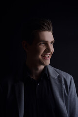 Obraz premium Studio portrait of a man with a raincoat on a black background. Muddy with a perfect hairstyle, European appearance posing, model in the side light. Smile