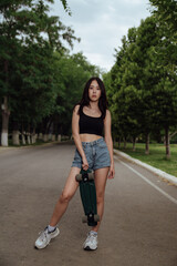 Young woman posing on street with skateboard in hands.