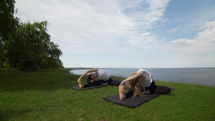 Two women meditating outdoors seated on the edge of coast near the sea, half lotus pose folded...
