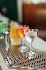 Several beautiful cocktails in nick and nora and highball glasses at the bar