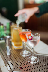 Several beautiful cocktails at the bar, bartender adding soda to one of them on the background