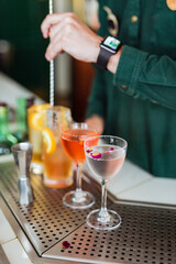Several beautiful cocktails at the bar, bartender stirring one of them on the background