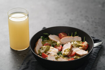 Salad with chicken, tomatoes, arugula and pesto in black bowl on concrete background