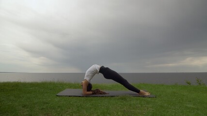 Young fit woman practice yoga on coast near the lake or sea. Woman doing Inverted Staff Dvi Pada Viparita Dandasana pose