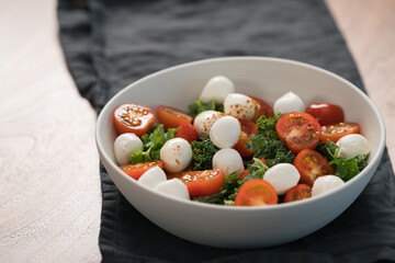 Salad with kale, tomatoes and mozzarella in white bowl