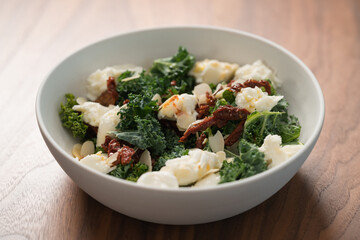 Salad with kale, sun-dried tomatoes and mozzarella in white bowl