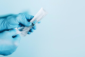 Hand in medical gloves holding syringe on blue background. Copy space. Injections and vaccination...