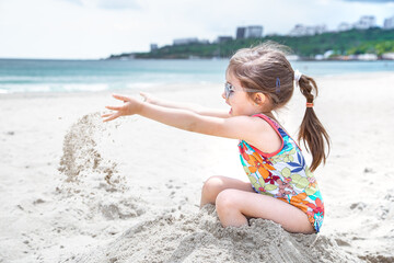 Little cute girl playing in the sand on the beach by the sea