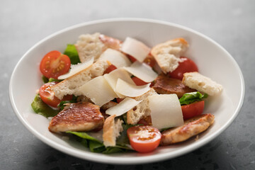 Fresh caesar salad with chicken and cherry tomatoes in white bowl