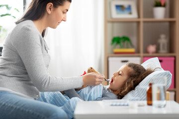 family, health and medicine concept - mother giving cough syrup to little sick daughter lying in bed at home
