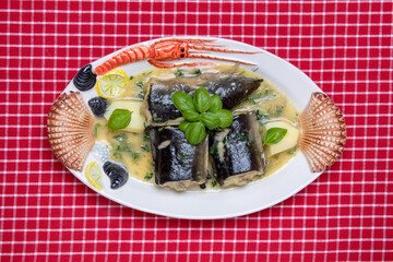 Fish dish top view. Close-up of freshly cooked pieces of European eel fish served on a porcelain plate with a creamy dill sauce and potatoes standing on a red tablecloth. Concept of delicious and heal