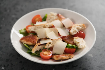 Fresh caesar salad with chicken and cherry tomatoes in white bowl