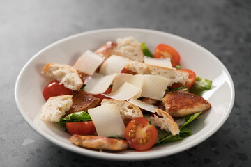 Fresh caesar salad with chicken and cherry tomatoes in white bowl