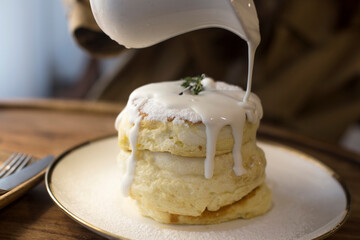 Souffle Pancakes served with syrup and fresh cream on white dish.