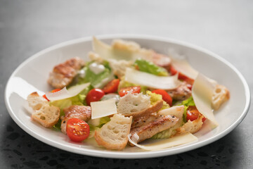 Fresh caesar salad with chicken and cherry tomatoes in white bowl