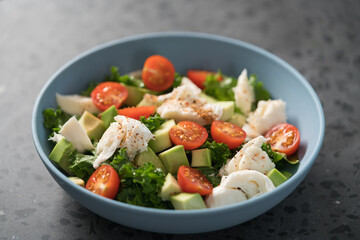 Salad with avocado, mozzarella, tomatoes and kale in blue ceramic bowl