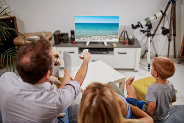 Family in isolation / quarantine looking at the sea beach on a TV. No travel this year?