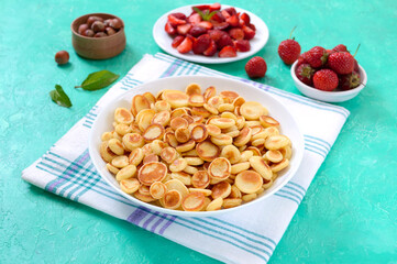 Pancake cereal in a bowl with fresh strawberries and nuts on a bright background. Tasty and trendy breakfast. Organic Dutch Mini-Pancakes. Foods trend.