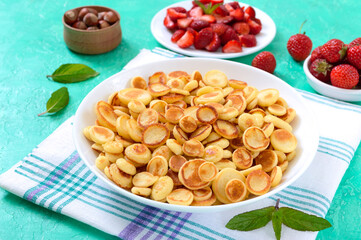 Pancake cereal in a bowl with fresh strawberries and nuts on a bright background. Tasty and trendy breakfast. Organic Dutch Mini-Pancakes. Foods trend.