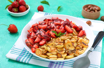 Pancake cereal in a bowl with fresh strawberries and nuts on a bright background. Tasty and trendy breakfast. Organic Dutch Mini-Pancakes. Foods trend.