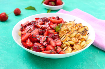 Pancake cereal in a bowl with fresh strawberries and nuts on a bright background. Tasty and trendy breakfast. Organic Dutch Mini-Pancakes. Foods trend.